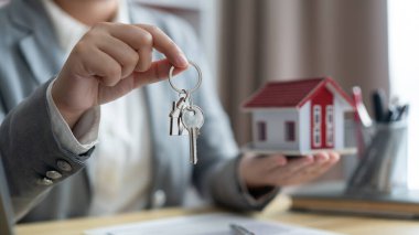 Sigorta konsepti. Emlak temsilcisi sağ elinde evin anahtarı, sol elinde de ev modeli tutuyor..