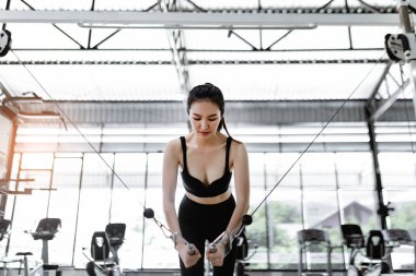 Egzersiz konsepti ayakta duran ve iki eliyle kıvrım çekme makinesine konsantre olan kadın..