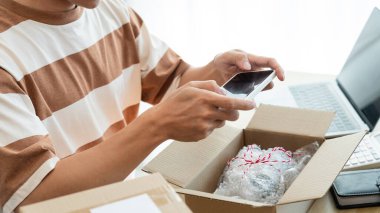 Çevrimiçi alışveriş konsepti. Tüccar cep telefonunu kullanarak ürününün kutuda fotoğrafını çekiyor..