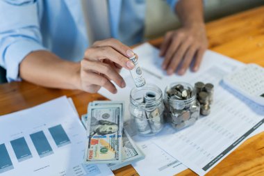 Tasarruf konsepti. Genç bir erkek parayı yuvarlıyor ve şişeye koyuyor..