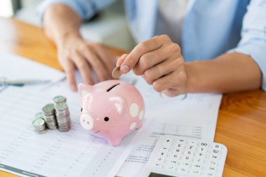 Tasarruf konsepti. Adam paraları masanın üzerine yığıyor ve kumbaraya bozuk para atıyor..