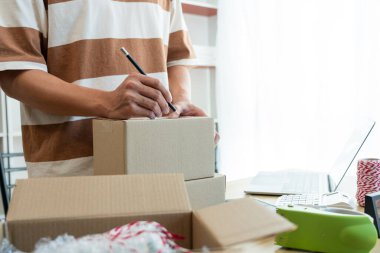 Çevrimiçi alışveriş kavramı. Satıcı paketin üzerine müşteri adresini yazıyor ve göndermeye hazır..