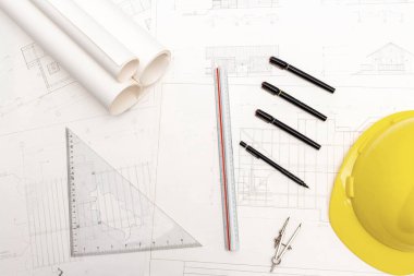 Mimari konseptin modeli, çizim araçları ve güvenlik kaskıyla plan üzerine çizim yapan mühendis.