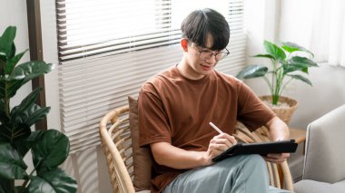 Teknoloji kavramı. Günlük tişörtü ve kotuyla rahat bir şekilde tahta koltukta oturan ve iPad 'deki web tarayıcısını kontrol etmek için dokunmatik ekran yapan erkek.