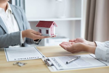 Sigorta konsepti. Emlakçı elinde bir ev modeli tutup müşterisine veriyor..