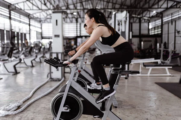 Egzersiz konsepti. İyi görünümlü bayan ve kaslı adam spor bisikletleri sürerken sohbet ederken eğleniyorlar..