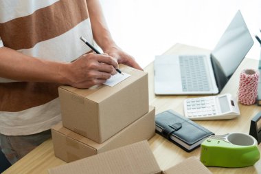 Çevrimiçi alışveriş konsepti. Ticari ajan ürünü paketlerken müşterilerinin bilgilerini kontrol etmek için akıllı telefonunu kullanıyor..