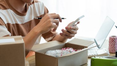 Çevrimiçi alışveriş konsepti. Ticari ajan ürünü paketlerken müşterilerinin bilgilerini kontrol etmek için akıllı telefonunu kullanıyor..
