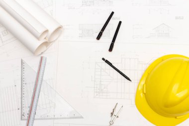 Mimari konseptin modeli, çizim araçları ve güvenlik kaskıyla plan üzerine çizim yapan mühendis.
