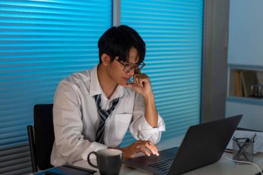 Fazla mesai. Ofis personeli masasında oturmuş, evrak okuyor ve not defterine yazı yazıyor.