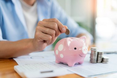 Tasarruf konsepti. Adam paraları masanın üzerine yığıyor ve kumbaraya bozuk para atıyor..