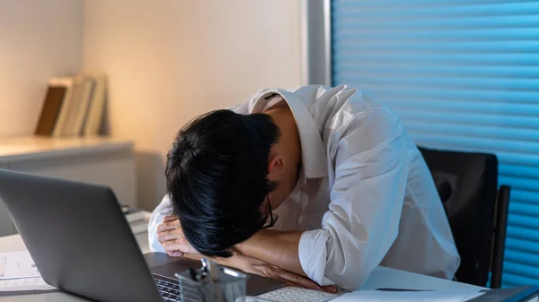 仕事の概念ノートパソコンの前で仕事をしながら机の上に頭を寝そべって仕事をする男 — ストック写真