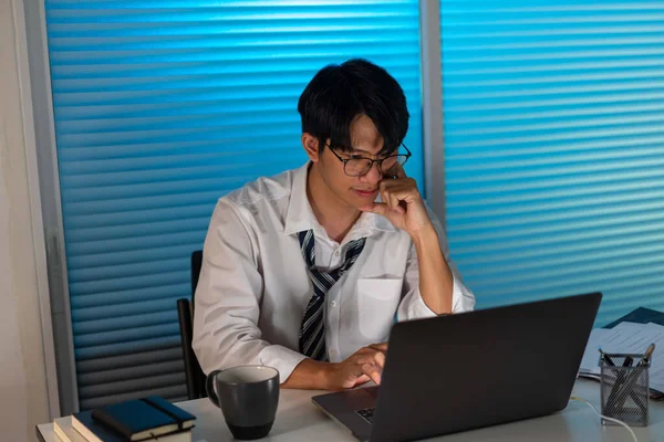 Fazla mesai. Ofis personeli masasında oturmuş, evrak okuyor ve not defterine yazı yazıyor.