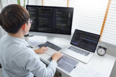 Yazılım geliştirme kavramı, veri kodu yazan ve birden fazla ekran üzerinde çalışan erkek programcı.