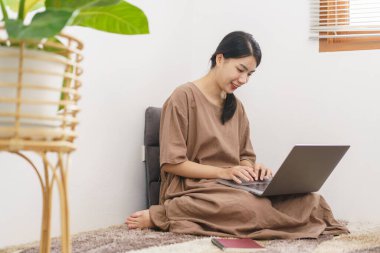 Rahatlama yaşam tarzı konsepti, genç Asyalı kadın evdeki oturma odasında eğlence için dizüstü bilgisayar kullanıyor..