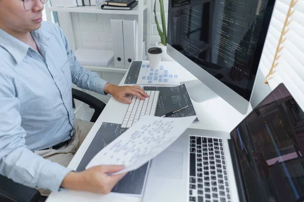 Software development concept, Male programmer read data on document while programming on computer.