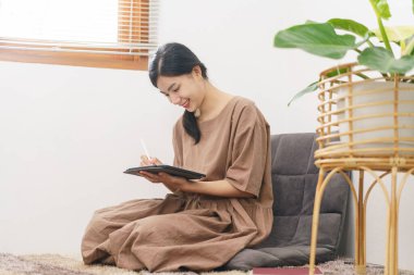 Rahatlama yaşam tarzı konsepti, genç Asyalı kadın oturma odasında otururken tablete yazıyor..