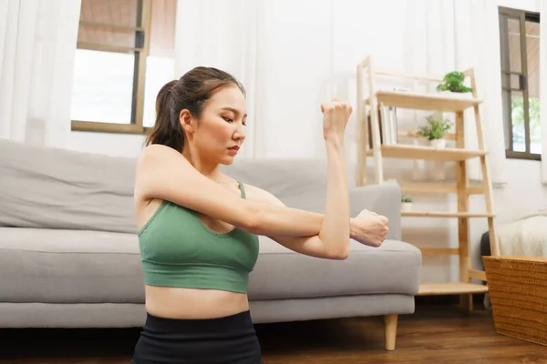 Yoga and wellness concept, Young Asian woman sit to stretching exercise arms on yoga mat at home.