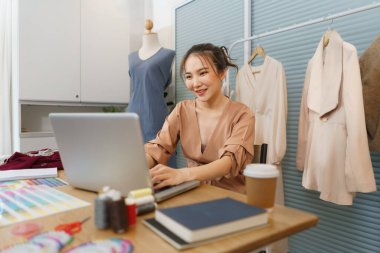 Moda tasarımı konsepti, Asyalı kadın tasarımcı yeni koleksiyon için veri aramak için dizüstü bilgisayar kullanıyor.