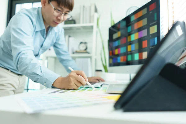Creativity concept, Male graphic designer choosing color swatch samples on document and designing.