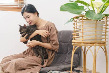 Evcil hayvan sevdalısı kavramı, genç Asyalı kadın koltukta oturup kediye sarılıyor ve oyun oynuyor..