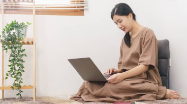 Rahatlama yaşam tarzı konsepti, genç Asyalı kadın evdeki oturma odasında eğlence için dizüstü bilgisayar kullanıyor..