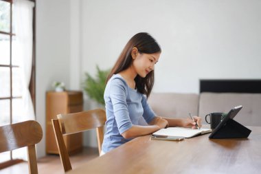 Work from home concept, Business women reads financial data on tablet and taking notes in notebook.