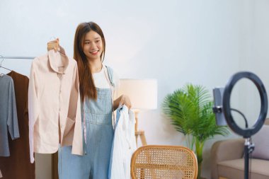 Online shopping concept, Young Asian women is selling and presents shirt detail in streaming video.