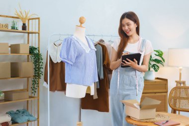 Online marketing concept, Asian women selling clothes in streaming video and check orders on tablet.