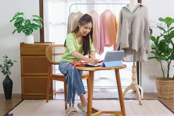 Fashion clothes merchant concept, Female seller measure size of dress and taking notes on notebook.