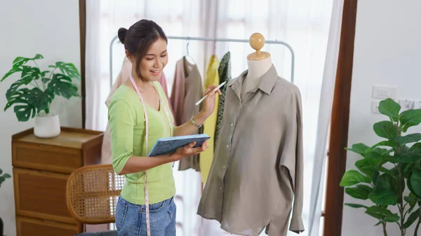 Fashion clothes merchant concept, Female designer checks detail of clothes and take notes on tablet.