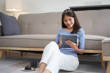 Work from home concept, Business women sit on the floor in living room and writing data on tablet.