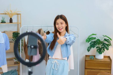 Online marketing concept, Young Asian women thumbs up while recommend clothes in streaming video.