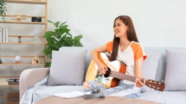 Guitar and singer concept, Young asian woman sitting on couch to playing music with acoustic guitar.