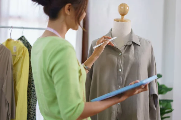 Fashion clothes merchant concept, Female designer checks detail of clothes and take notes on tablet.