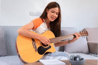 Hobi konsepti, akustik gitarla şarkı söyleyen ve çalan genç bir kadın şarkı sözleri okurken..