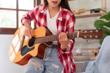 Müzikle rahatlama kavramı, genç Asyalı kadın akustik gitarla akorlar çalmaya çalışıyor..
