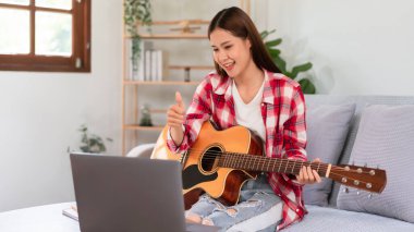 Hobi konsepti, genç Asyalı kadın canlı yayında akustik gitar çalıyor ve baş parmak hareketi yapıyor..