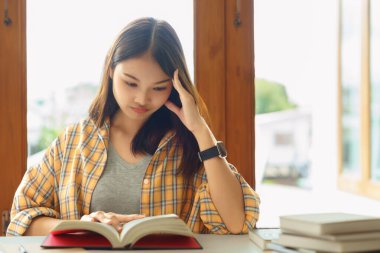 Eğitim ve okur yazarlık kavramı, üniversite öğrencisi kız kütüphanede kitap okurken kafası karışıyor.