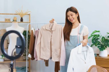Online shopping concept, Young Asian women is selling and presents shirt detail in streaming video.