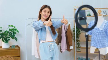 Moda blogcusu konsepti, genç Asyalı kadınlar başparmağını kaldırırken videoda kıyafet öneriyor.