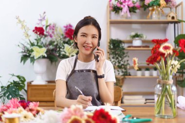 Çiçekçi kavramı, kadın çiçekçinin müşteriyle telefonda konuşması ve mağazadaki not defterine not alması..