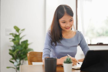 Work from home concept, Business women taking notes while reads data on tablet in living room.
