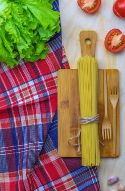 Spagetti ve kırmızı domatesler kırsal bir ahşap masanın üzerinde yatıyor.