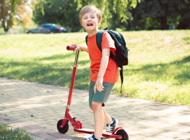 Küçük çocuk ağlıyor. O bir scooter tutuyor. Kırmızı tişörtlü yeşil çimenli bir çocuk.