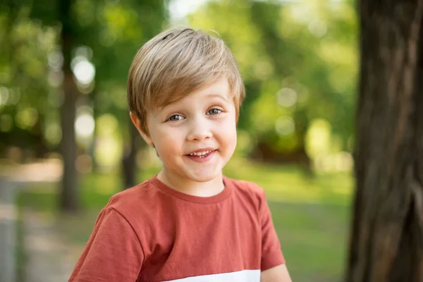Radosny chłopczyk. Uśmiecha się na tle zielonego parku. Chłopiec patrzy w obiektyw kamery. — Zdjęcie stockowe