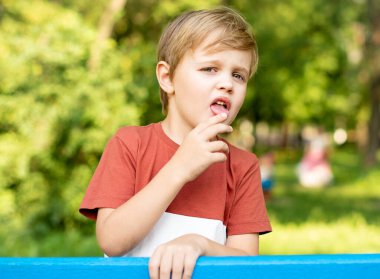 Yeşil Park 'ın arka planında güzel ve ciddi bir çocuğun portresi. O, mavi çitin yanında duruyor. Adam çok düşünceli görünüyor.