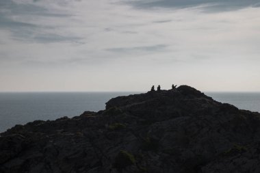 Deniz manzarası bazı insanları bulutlu bir gökyüzünün altındaki kayalık bir dağın tepesinde akşam vakti Katalonya 'daki Costa Brava' daki Cap de Creus Burnu 'nda gösteriyor.