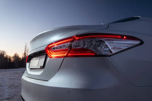 Modern beyaz arabanın LED kırmızı arka lambasının detaylı görüntüsünü kapat. Yeni otomobilin dış detayları. Akşam sokak otoparkında çekilen kış fotoğrafı.