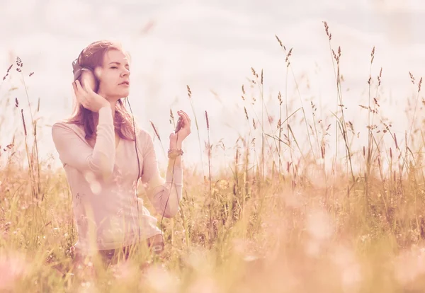 Background girl with headphones sitting in the grass in the fiel — Stock Photo, Image